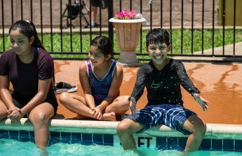 Three kids sitting by an outdoor pool